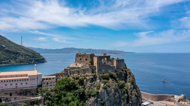 Scilla - Kalabrien - 05-27-2025: Tarihi Castello Ruffo di Scilla sakin denizin üzerindeki kayalık uçurum, mavi gökyüzü, Calabria, İtalya 'daki kıyı şeridi ve uzak tepelerle çevrili.