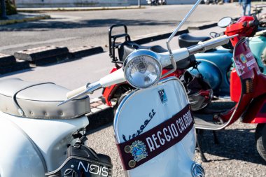 Reggio Calabria - Kalabrien - 05-18-2025: Reggio Calabria kulüp afişi ile klasik beyaz Vespa Üstün Centilmenler Biniş etkinliğinde mobiletlerin arasına park edilmiş.