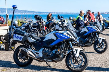 Reggio Calabria - Kalabrien - 05-18-2025: Polizia Locale damgalı iki polis motosikleti, çeşitli motosikletler ve güpegündüz insanlarla çevrili deniz kenarında park halinde.