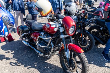 Reggio Calabria - Kalabrien - 05-18-2025: Aralarında görünür kasklı kırmızı bir Royal Enfield ve yakınlarda duran insanların da bulunduğu bir etkinlikte çok sayıda motosiklet birbirine yakın park edilmiş durumda.