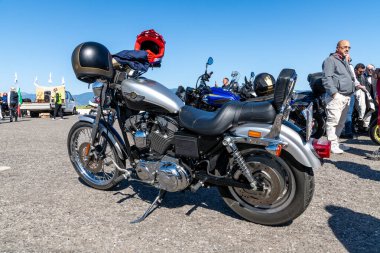 Reggio Calabria - Kalabrien - 05-18-2025: Kırmızı ve siyah kasklı gümüş bir motosiklet, açık bir günde motosikletliler ve park halindeki diğer motosikletlerle çevrili bir motosiklet etkinliğine park edildi.
