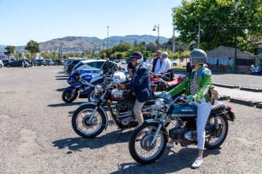 Reggio Calabria - Kalabrien - 05-18-2025: Reggio Calabria, İtalya 'daki Seçkin Beyefendiler Turu sırasında park alanında klasik bisiklet ve kasklı motosikletçiler.