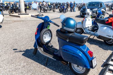 Reggio Calabria - Kalabrien - 05-18-2025: Seçkin beyefendiler Reggio Calabria 'ya giderken çekildi, kaskı ve yedek lastiği olan mavi bir Vespa sergileniyor..