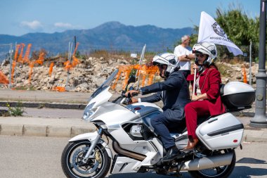 Reggio Calabria - Kalabrien - 05-18-2025: Kasklı bir erkek ve kadın güneşli bir günde Reggio Calabria 'da düzenlenen Üstün Beyefendiler Turu sırasında beyaz bir motosiklete biniyorlar.