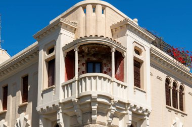 Reggio Calabria - Kalabrien - 05-22-2025: Yuvarlak kolonlar, kemerli detaylar ve mavi gökyüzünün altında üst kattaki tarihi binanın ön cephesinde kırmızı desenli bir duvar ile süslü köşe balkonu.