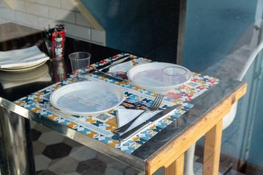 Reggio Calabria - Kalabrien - 05-22-2025: Reggio Calabria 'da tek kullanımlık plakalar, plastik bardaklar ve yansıtıcı bir pencerenin arkasındaki renkli kaplara yerleştirilmiş restoran masası.