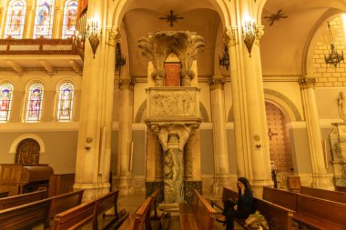 Reggio Calabria - Kalabrien - 05-22-2025: Bir katedralin içindeki mermer kürsüde heykel kabartmaları, oyulmuş hayvanlar ve sütunlar ve kemerler tarafından çerçevelenmiş kırmızı bir koltuk yer alıyor..