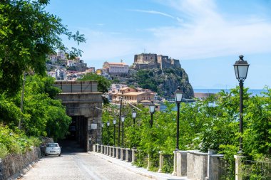Scilla - Kalabrien - 05-27-2025: Scilla, Calabria 'daki Castello Ruffo manzarası, lamba direkli yol, yamaçlı binalar, kıyı manzarası ve arka planda mavi deniz.