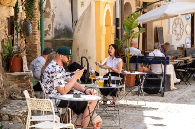 Scilla - Kalabrien - 05-27-2025: Birkaç kişi Scilla, Calabria 'daki bir kafenin önündeki açık hava masalarında oturmuş, yemek yiyor, içiyor ve gün ışığında konuşuyor