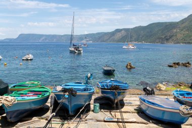 Scilla - Kalabrien - 05-27-2025: Scilla, Calabria körfezinde demirli balıkçı tekneleri ve yatlar, arka planda dağlar ve kıyıya yakın açık sığ sular.