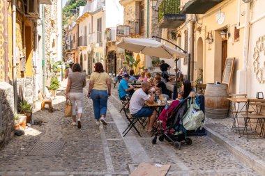 Scilla - Kalabrien - 05-27-2025: Scilla, Calabria 'da, insanlar kafeler, masalar ve geleneksel taş binalarla dolu dar bir kaldırımda yemek yiyor ve geziniyorlar.....