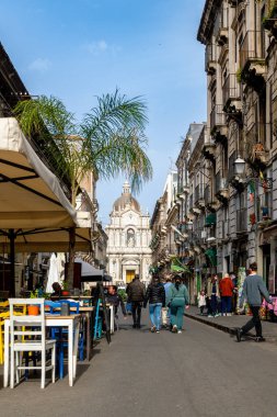Catania, Sizilien - İtalya - 04-15-2025: Catania, Sicilya 'da sokak sahnesi, renkli açık hava oturma yerleri, palmiye ağaçları, tarihi binalar ve arka planda barok bir kilise kubbesi.