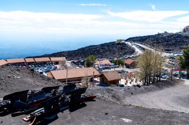 Catania, Sizilien - İtalya - 04-22-2025: Açık mavi gökyüzü altında Etna Dağı ana kampı üzerinde park alanları, hediyelik eşya dükkanları, dolambaçlı erişim yolu ve volkanik arazi.