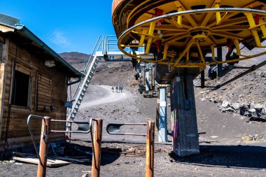 Catania, Sizilien - İtalya - 04-22-2025: Paslı metal yapısı, ahşap kulübesi, volkanik arazisi, yürüyüşçüleri ve açık mavi gökyüzü olan Etna Dağı 'ndaki kırık teleferik istasyonu.