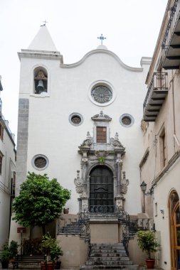 Cefalu - Sizilien - Italien - 03-24-2025: Cefalu 'daki Santo Stefano kilisesinin ön manzarası, bir çan kulesi, dekoratif giriş kapısı ve demir detaylarla çevrili yuvarlak pencereler.