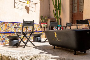 Tropea - Kalabrien - İtalya - 05-30-2025: Tropea, Calabria 'daki açık avlu, renkli fayanslı banklar, siyah sandalyeler ve güneş ışığı altında yeniden tasarlanmış bir küvet.