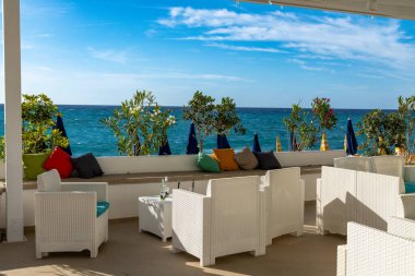 Tropea - Kalabrien - İtalya - 05-30-2025: Wicker koltukları Tropea, Calabria 'da, gölgeli bir terasın altında, yastıklar, saksılar ve kapalı plaj şemsiyeleri ile denize bakıyor.