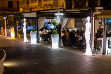 Tropea - Kalabrien - İtalya - 05-30-2025: İnsanlar Haziran 2025 'te bir yaz akşamı Tropea, Calabria, İtalya' da bir kokteyl bar terasında aydınlatılmış süslemelerle yemek yiyor.