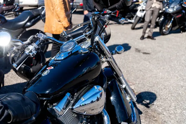 Reggio Calabria - Kalabrien - 05-18-2025: Krom detaylı siyah kruvazör motosikleti, tank üzerinde görünür olay çıkartmaları ve arka planda motosikletlerin yanında duran insanlar.