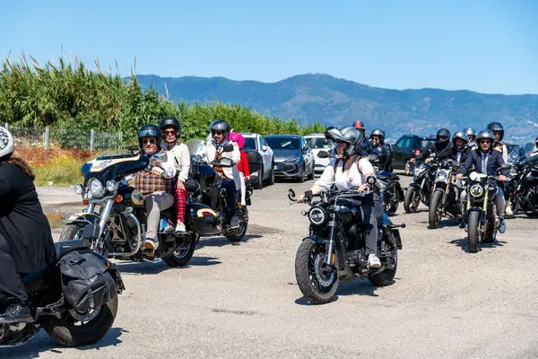 Reggio Calabria - Kalabrien - 05-18-2025: Bir grup motosikletçi, güneşli bir günde park halindeki arabaları ve yeşil tepeleri olan seçkin beyefendilere katılıyor.
