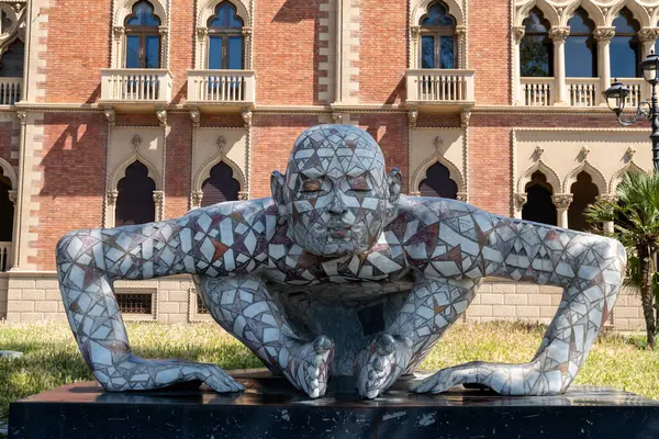 Reggio Calabria - Kalabrien - 05-22-2025: Mozaik heykel Co-stell-azione tarihi binanın ön cephesinde çömelmiş bir erkek figürü gösteriyor.