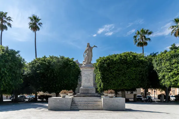 Reggio Calabria - Kalabrien - 05-22-2025: Açık mavi gökyüzü altında, Reggio Calabria 'da ağaçlar ve palmiyelerle basamaklı bir üste mermer heykeli olan Plaza.