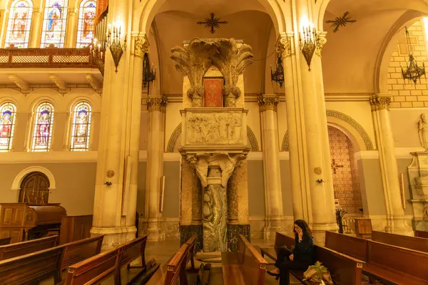 Reggio Calabria - Kalabrien - 05-22-2025: Bir katedralin içindeki mermer kürsüde heykel kabartmaları, oyulmuş hayvanlar ve sütunlar ve kemerler tarafından çerçevelenmiş kırmızı bir koltuk yer alıyor..