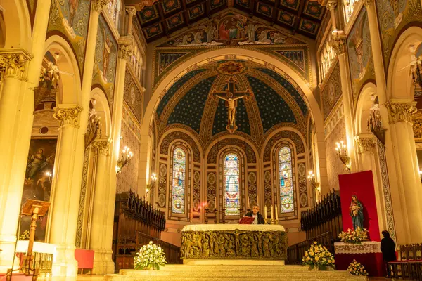 Reggio Calabria - Kalabrien - 05-22-2025: Sütunlar, çiçek düzenlemeleri ve dini dekorasyonlarla çevrili, haçlı ve renkli vitraylı sunaktaki adam.