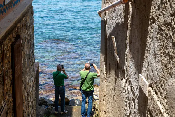 Scilla - Kalabrien - 05-27-2025: Dar taş binaların arasında duran iki adam, Scilla, Calabria 'daki açık denizi duvar dokusu ve kıyı detaylarıyla fotoğraflıyor.
