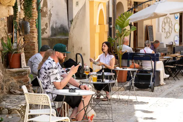 Scilla - Kalabrien - 05-27-2025: Birkaç kişi Scilla, Calabria 'daki bir kafenin önündeki açık hava masalarında oturmuş, yemek yiyor, içiyor ve gün ışığında konuşuyor