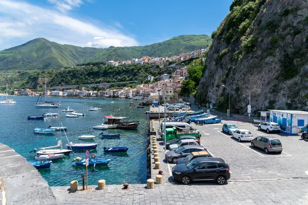 Scilla - Kalabrien - 05-27-2025: Arka planda kıyı köyü ve yeşil dağları bulunan sarp bir yamacın yanındaki bir marinada çeşitli tekneler yüzüyor.