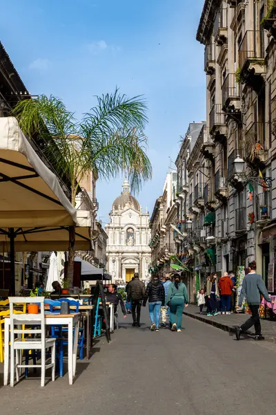 Catania, Sizilien - İtalya - 04-15-2025: Catania, Sicilya 'da sokak sahnesi, renkli açık hava oturma yerleri, palmiye ağaçları, tarihi binalar ve arka planda barok bir kilise kubbesi.