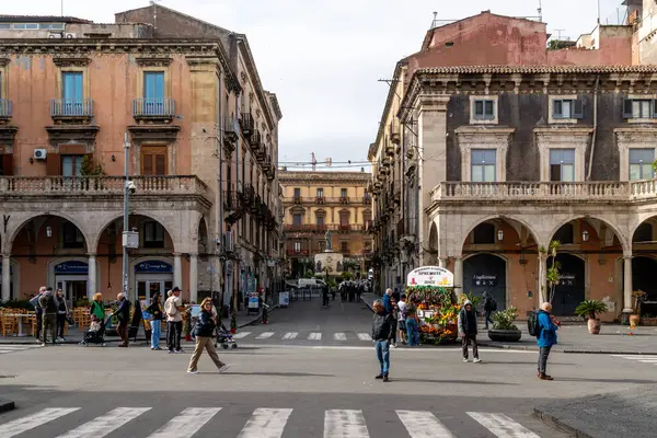 Catania, Sizilien - İtalya - 04-15-2025: Yayalar, tarihi binalar ve zarif bir mimari arkaplan önündeki meyve suyu standı ile dolu şehir meydanı.