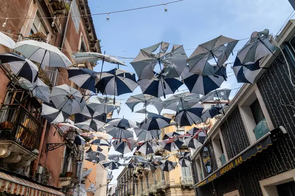 Catania, Sizilien - İtalya - 04-15-2025: Catania 'da bir caddenin karşısına binalar ve balkonlar arasında uzanan çok sayıda şemsiye asılarak renkli bir tepe örtüsü oluşturuluyor.