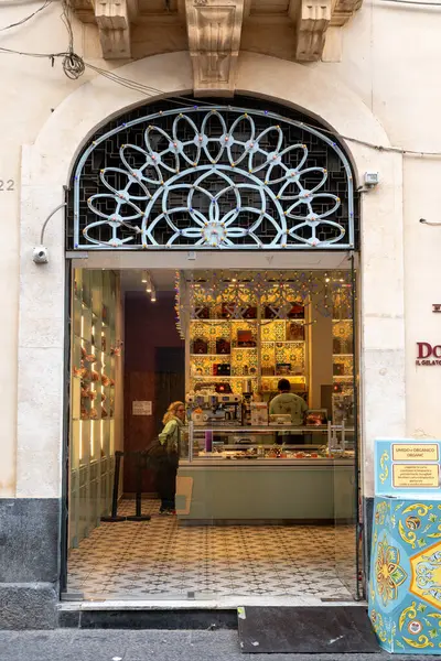 Catania, Sizilien - İtalya - 04-15-2025: Catania, Sicilya 'da renkli fayanslı bir gelato dükkanının içi, bir tatlı tezgahı, bir cam kapı girişi ve içeride bir müşteri.