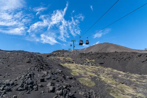 Catania, Sizilien - İtalya - 04-22-2025: Etna teleferikleri koyu volkanik arazide kayarak taşlarla ve otlarla kaplı, parlak mavi gökyüzü altında ince beyaz bulutlar altında.