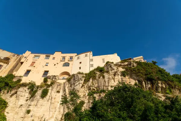 Tropea - Kalabrien - İtalya - 05-29-2025: Tropea, Calabria 'daki binalar, üzerinde açık mavi bir gökyüzü ve kayalık yamacı aydınlatan sıcak güneş ışığıyla dik bir uçurumun tepesinde duruyor.