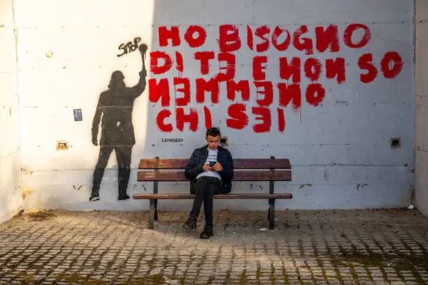 Tropea - Kalabrien - İtalya - 05-29-2025: Bir adam bir bankta oturuyor ve sana ihtiyacım olduğunu söylüyor ve kalın harflerle kim olduğunu bile bilmiyorum..