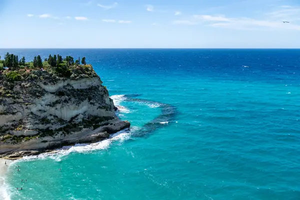 Tropea - Kalabrien - İtalya - 05-30-2025: Turkuaz deniz, Calabria 'daki Tropea' daki kayalıkları görünür bir kıyı şeridi, kayalık çıkıntısı ve aşağıda yüzen insanlarla çevreler..