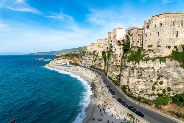 Tropea - Kalabrien - İtalya - 05-30-2025: Tropea, Calabria, İtalya 'daki plaja ve Tyrhenian Denizi' ne tepeden bakan kayalık binalar açık mavi gökyüzü ve kalabalıklarla güneşli bir öğleden sonra.