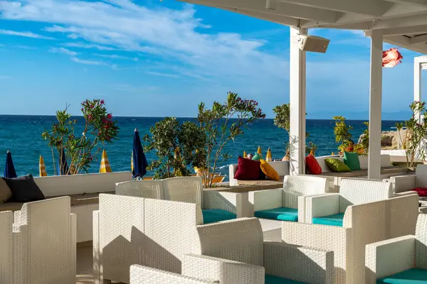 Tropea - Kalabrien - İtalya - 05-30-2025: Beyaz hasır sandalyeler ve renkli yastıklar Tropea, Calabria, İtalya 'daki berrak mavi denize bakan teras çatısı altında düzenleniyor.