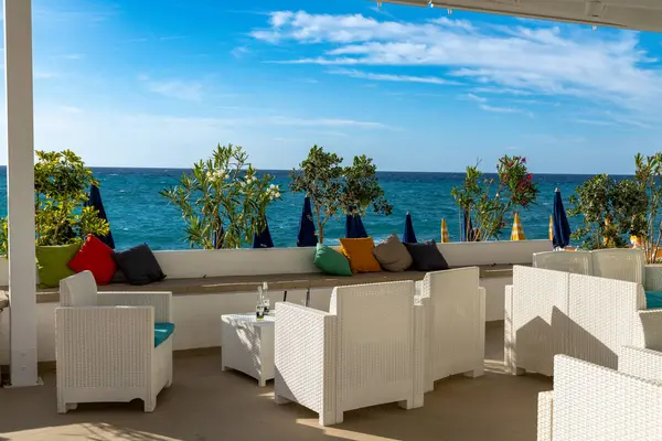 Tropea - Kalabrien - İtalya - 05-30-2025: Wicker koltukları Tropea, Calabria 'da, gölgeli bir terasın altında, yastıklar, saksılar ve kapalı plaj şemsiyeleri ile denize bakıyor.