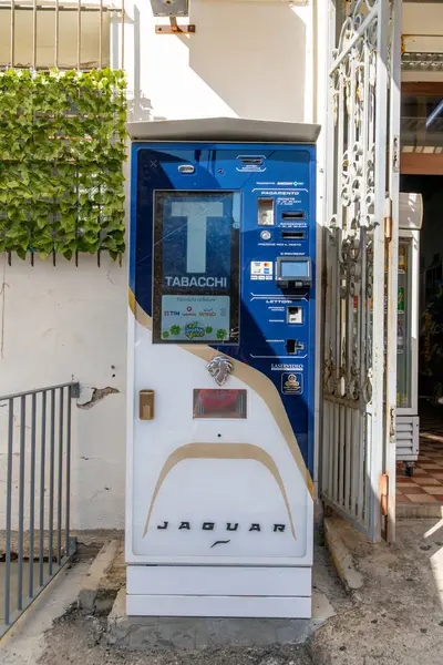 Pizzo - Kalabrien - İtalya - 06-02-2025: Pizzo, İtalya 'da açık hava tütün otomatı, parlak gün ışığında yeşil sarmaşıklı bir kapı ve duvarın yanında yer alıyor.