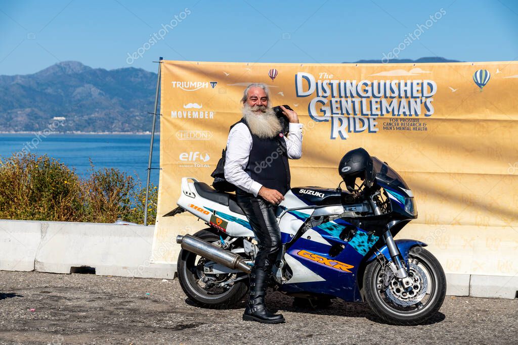 Reggio Calabria - Kalabrien - 05-18-2025: Man with long beard posing beside Suzuki GSX-R during the Distinguished Gentlemans Ride in Reggio Calabria, with sponsor banner behind him.