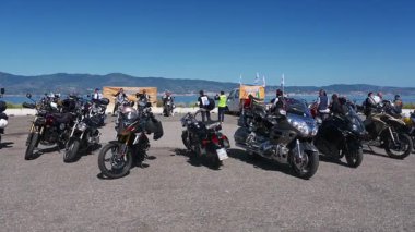 Geniş açılı çekimde Reggio Calabria 'da motosiklet ve biniciler görülüyor. Seçkin beyefendiler mavi gökyüzünün altındaki bir sahil parkında geziyorlar..