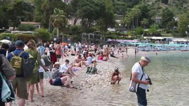 Taormina 'daki kalabalık bir yaz sahnesinde Isola Bella' da yüzücüler görülüyor. Kamera yavaşça açık denize doğru dönüyor..