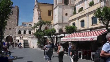 İnsanlar Taormina 'daki Piazza IX Aprile' de yürürken kamera yavaşça yukarı doğru San Giuseppe kilisesinin tarihi kulesine doğru kayıyor..