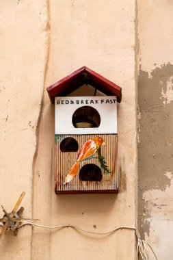 Taranto - Puglia - Italien - 06-17-2025: A painted wooden birdhouse mounted on a wall, labeled Bed and Breakfast with a colorful bird illustration and visible round entrances.