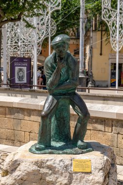 Matera - Basilikata - Italien - 06-16-2025: İtalya 'nın Matera kentinde oturan düşünceli bir adamın bronz heykeli, gün ışığında binalar ve ziyaretçiler önünde net bir şekilde fotoğraflandı.