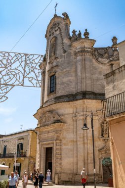 Matera - Basilikata - Italien - 06-16-2025: Matera, Basilicata, İtalya 'daki süslü taş cepheli Barok Kilisesi, mavi gökyüzü altında güneşli bir yaz günü turistler tarafından ziyaret edildi.